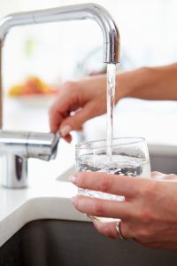 Close Up Of Woman Pouring Glass Of Water From Tap In Kitchen